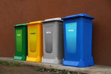 Photo of Many color recycling bins near brown wall outdoors