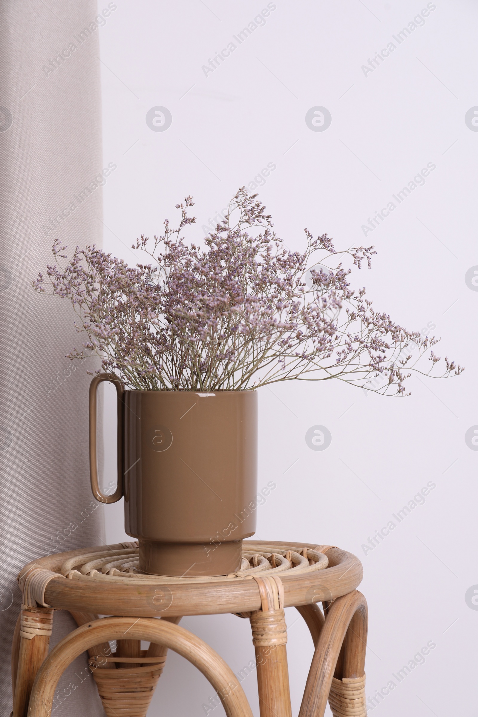 Photo of Ceramic vase with dry flowers on wicker table near white wall