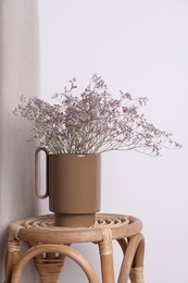 Photo of Ceramic vase with dry flowers on wicker table near white wall