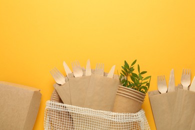 Flat lay of paper and wooden tableware with green twigs on yellow background, space for text. Eco friendly lifestyle
