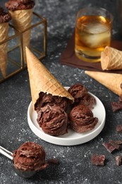 Photo of Tasty ice cream scoops, chocolate crumbs and waffle cones on dark textured table, closeup