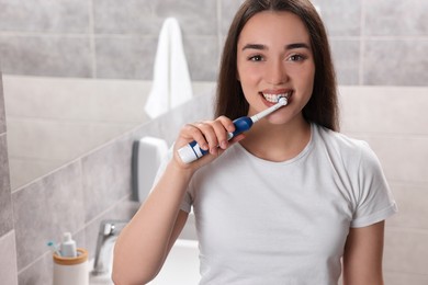 Young woman brushing her teeth with electric toothbrush in bathroom