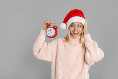 Photo of Woman in Santa hat with alarm clock on grey background. New Year countdown