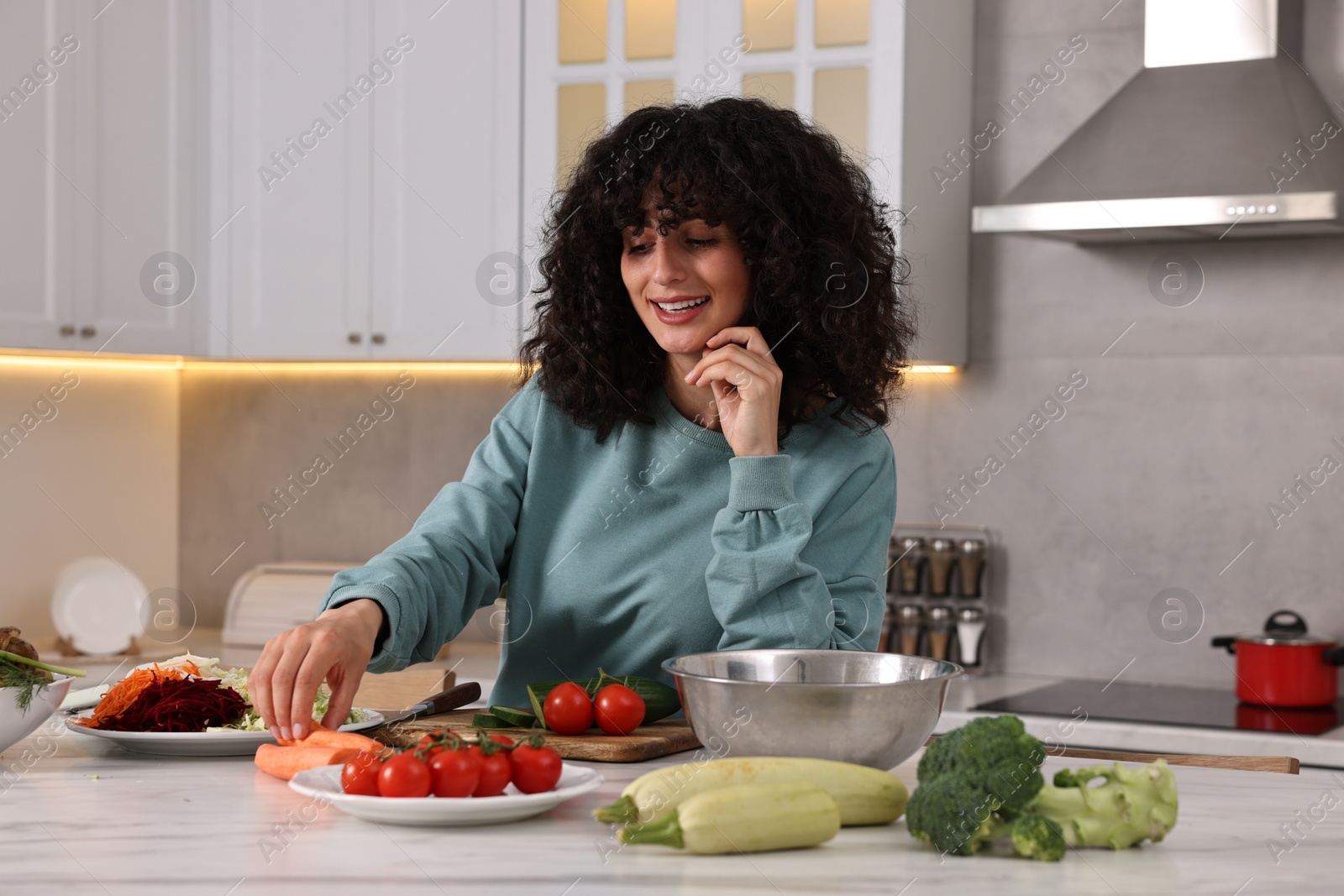 Photo of Woman cooking healthy vegetarian meal at white marble table in kitchen