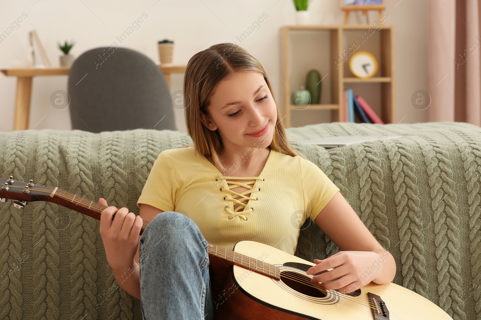 Photo of Teenage girl playing acoustic guitar near bed in room