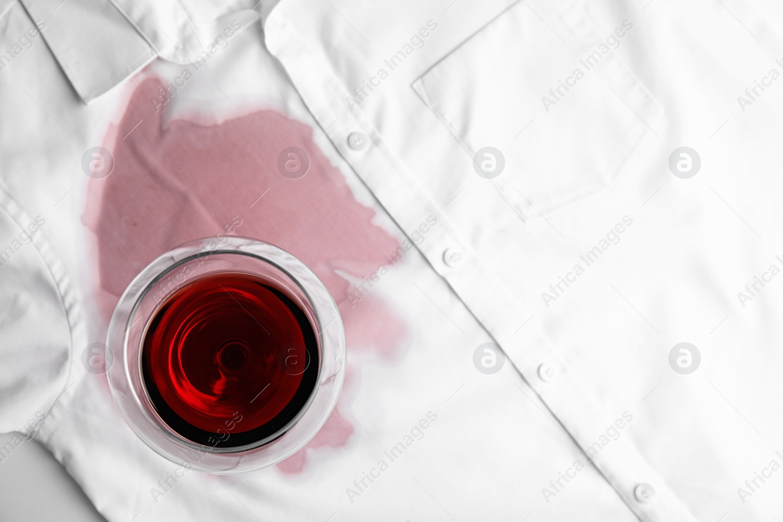 Photo of Transparent glass and spilled exquisite red wine on white shirt, top view. Space for text