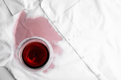 Photo of Transparent glass and spilled exquisite red wine on white shirt, top view. Space for text