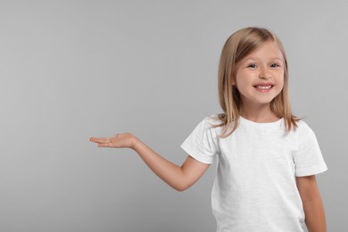 Photo of Special promotion. Smiling girl showing something on grey background. Space for text