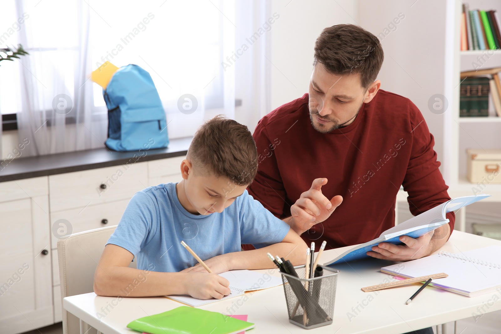 Photo of Dad helping his son with homework in room