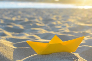 Beautiful yellow paper boat on sand outdoors, closeup