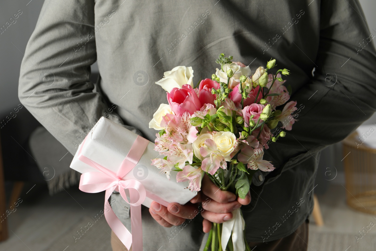 Photo of Man hiding bouquet of flowers and present indoors, closeup