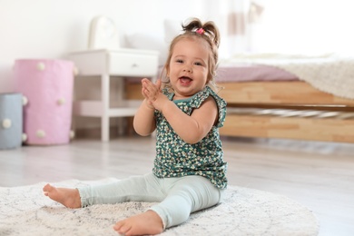 Photo of Adorable little baby girl sitting on floor in room