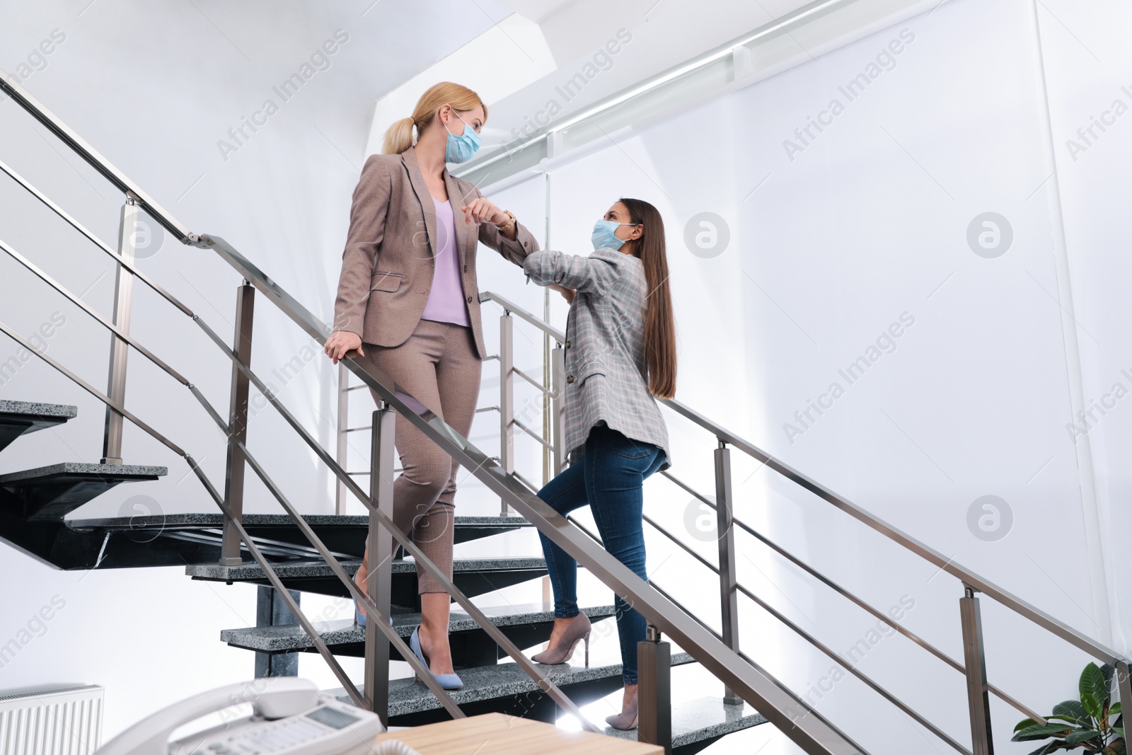 Photo of Office employees in masks greeting each other by bumping elbows on stairs