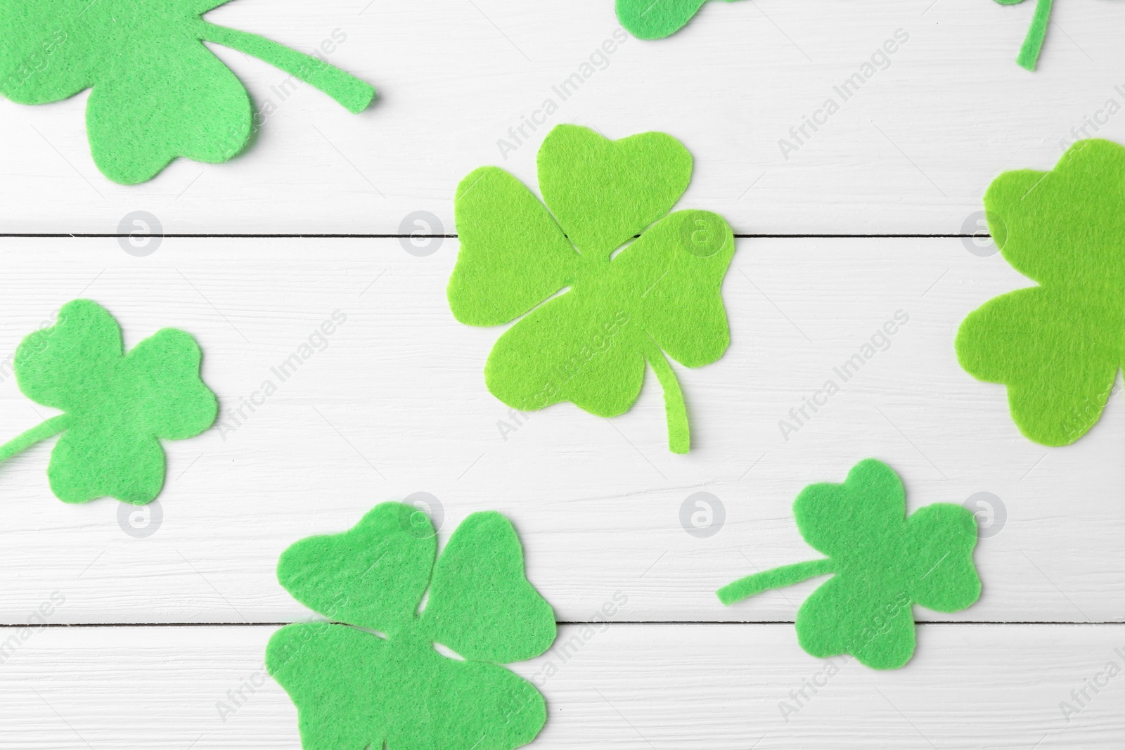 Photo of St. Patrick's day. Decorative green clover leaves on white wooden table, flat lay