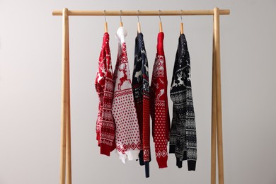 Different Christmas sweaters hanging on rack against light background