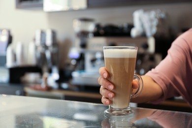 Barista putting glass with delicious coffee on countertop in cafe, space for text