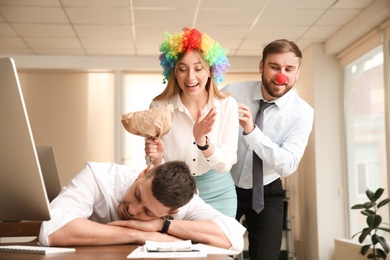 Photo of Coworkers popping paper bag behind their sleeping colleague in office. Funny joke