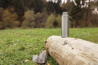 Metallic thermos on log outdoors, space for text