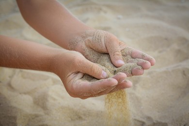 Photo of Child pouring sand from hands on beach, closeup. Fleeting time concept