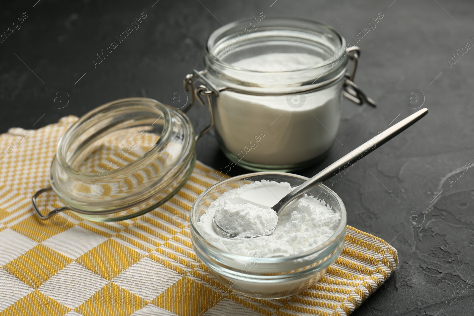 Photo of Baking powder in bowl, jar and spoon on black textured table, closeup