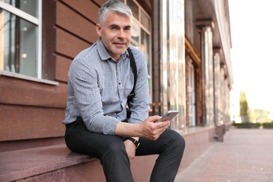 Photo of Portrait of handsome businessman with mobile phone in city, space for text