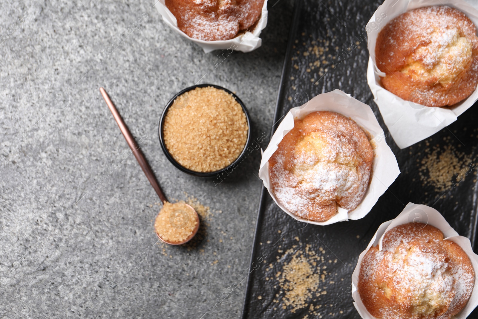 Photo of Delicious muffins and sugar on grey table, flat lay