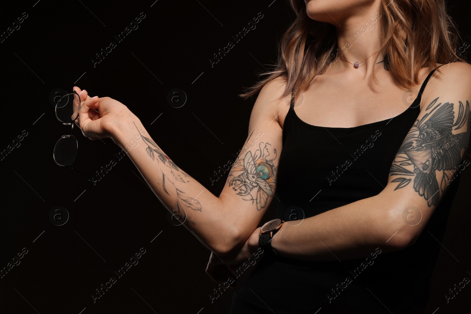 Photo of Beautiful woman with tattoos on body against black background, closeup