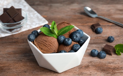 Photo of Bowl of chocolate ice cream and blueberries served on wooden table, space for text