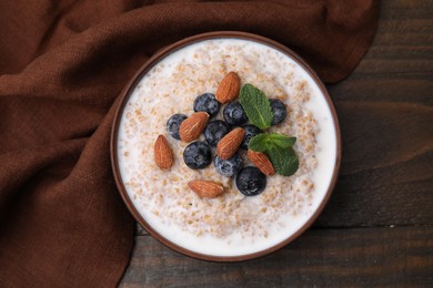 Tasty wheat porridge with milk, blueberries and almonds in bowl on wooden table, top view