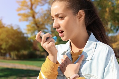 Photo of Young woman using asthma inhaler outdoors. Space for text