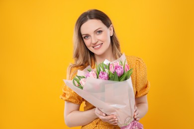 Happy young woman with bouquet of beautiful tulips on yellow background