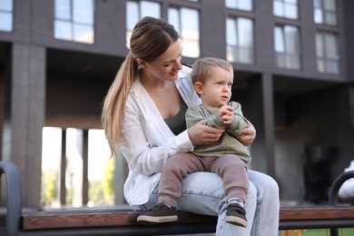 Beautiful nanny with cute little boy on bench outdoors,