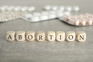 Photo of Word Abortion made of wooden cubes and pills on grey table, closeup