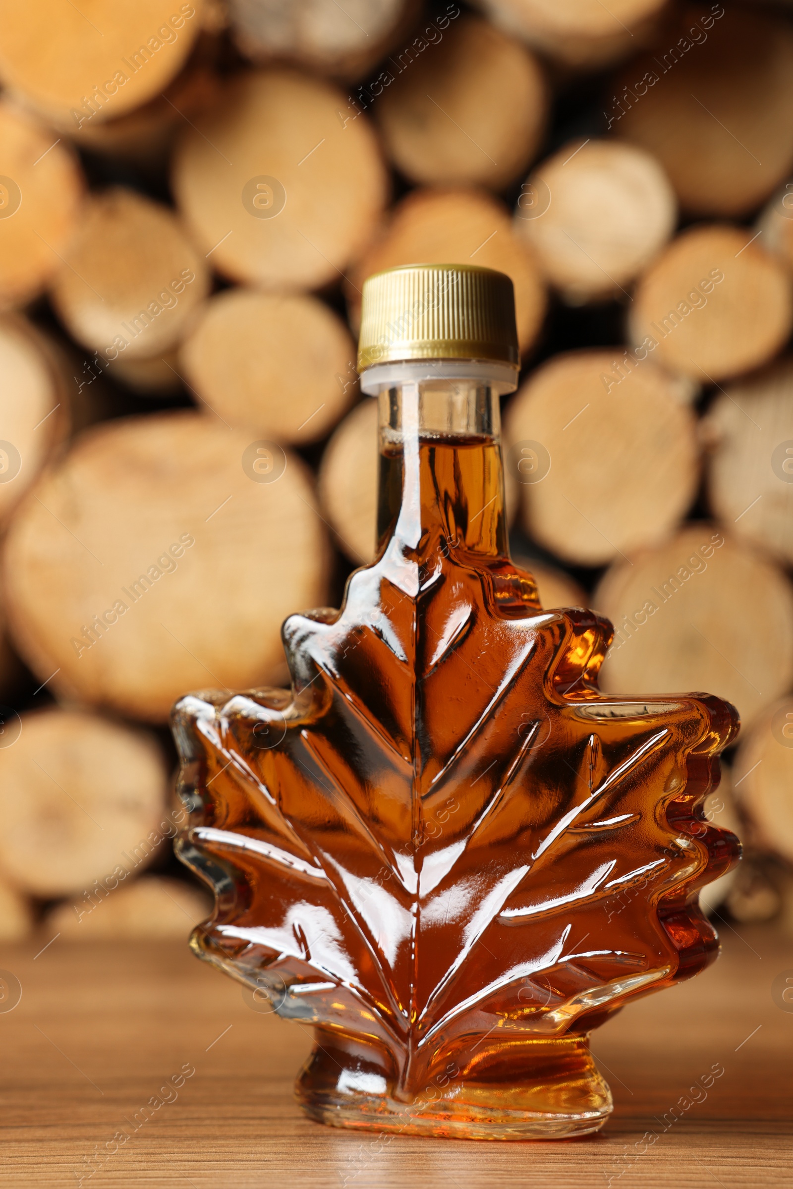 Photo of Leaf shaped bottle of tasty maple syrup on wooden table