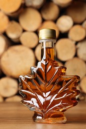 Leaf shaped bottle of tasty maple syrup on wooden table