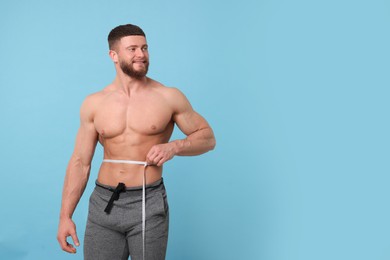 Photo of Portrait of happy athletic man measuring waist with tape on light blue background, space for text. Weight loss concept