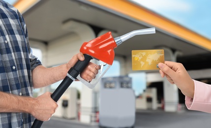 Image of Woman holding credit card and worker with fuel nozzle at gas station, closeup. Cashless payment