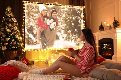 Image of Woman with cup of hot drink watching romantic movie via video projector in room. Cozy winter holidays atmosphere