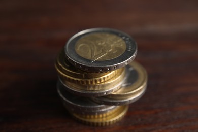 Photo of Many Euro coins stacked on wooden table, closeup