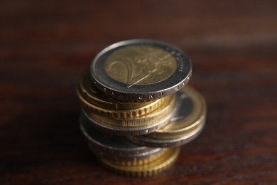 Many Euro coins stacked on wooden table, closeup