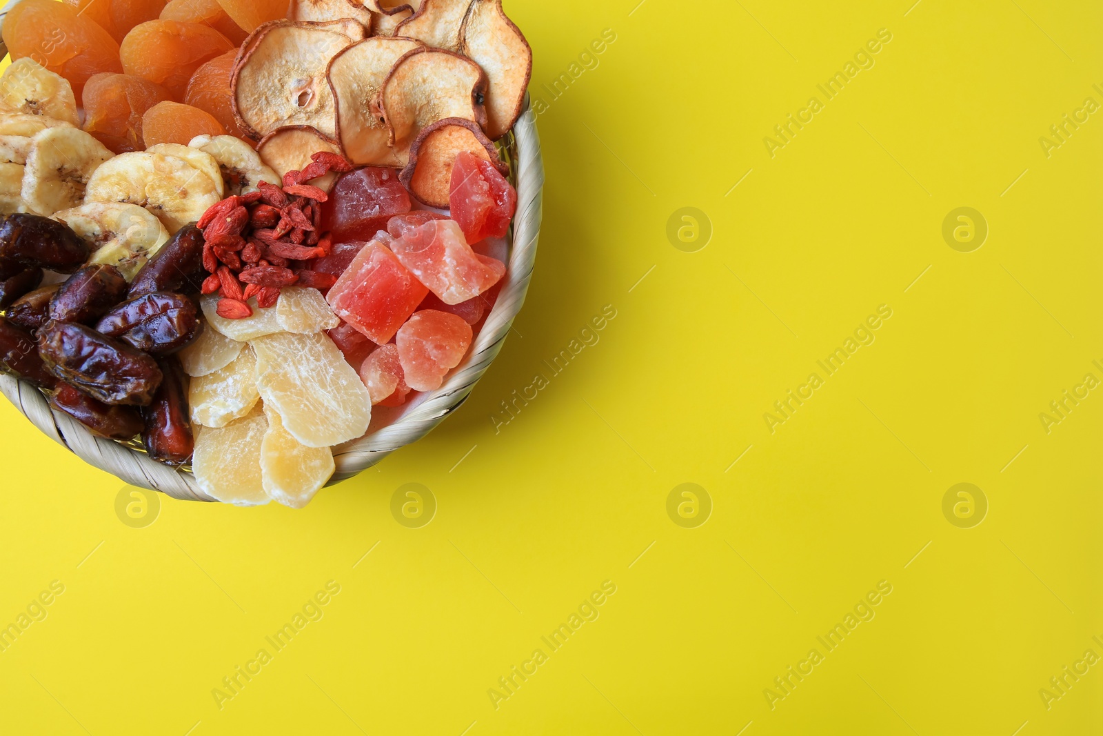 Photo of Wicker basket with different dried fruits on yellow background, top view. Space for text