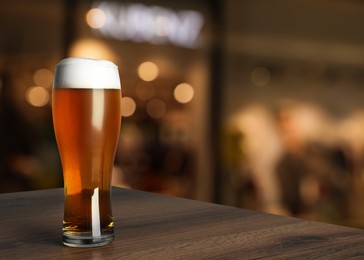 Image of Glass with cold tasty beer on wooden table in pub, space for text