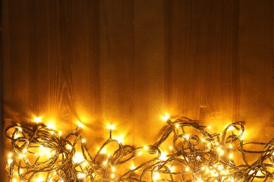 Beautiful bright Christmas lights on wooden background, flat lay. Space for text