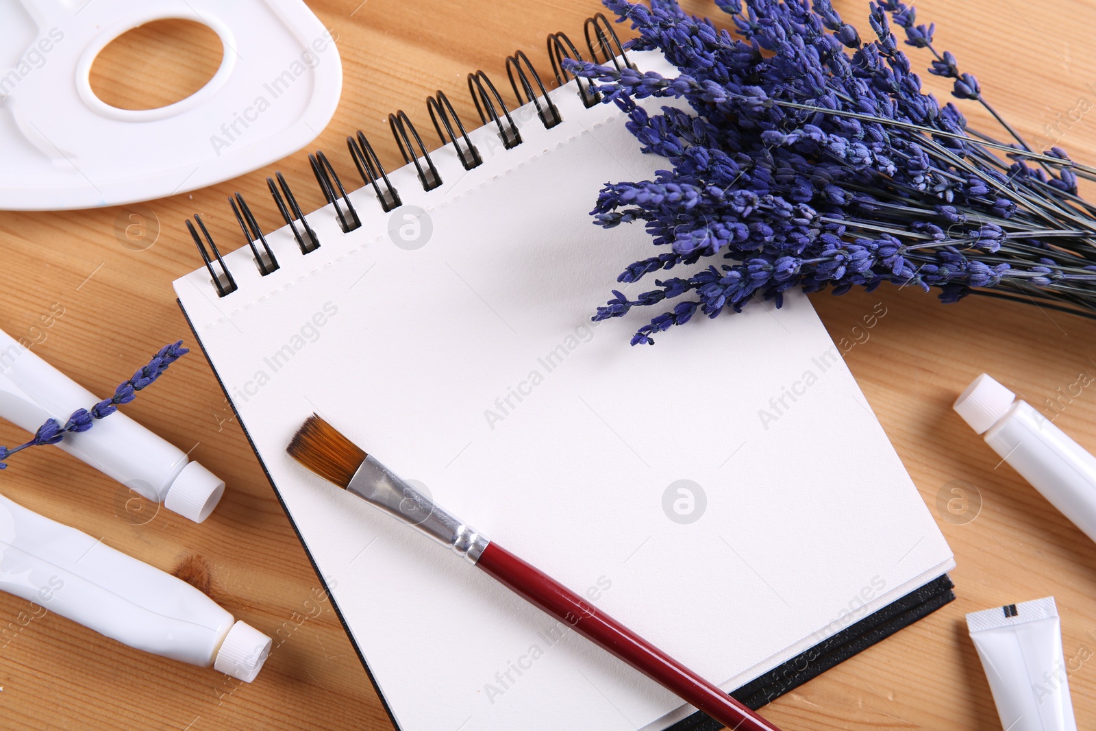 Photo of Bouquet of beautiful preserved lavender flowers, notebook, palette, brush and paints on wooden table, flat lay. Space for text