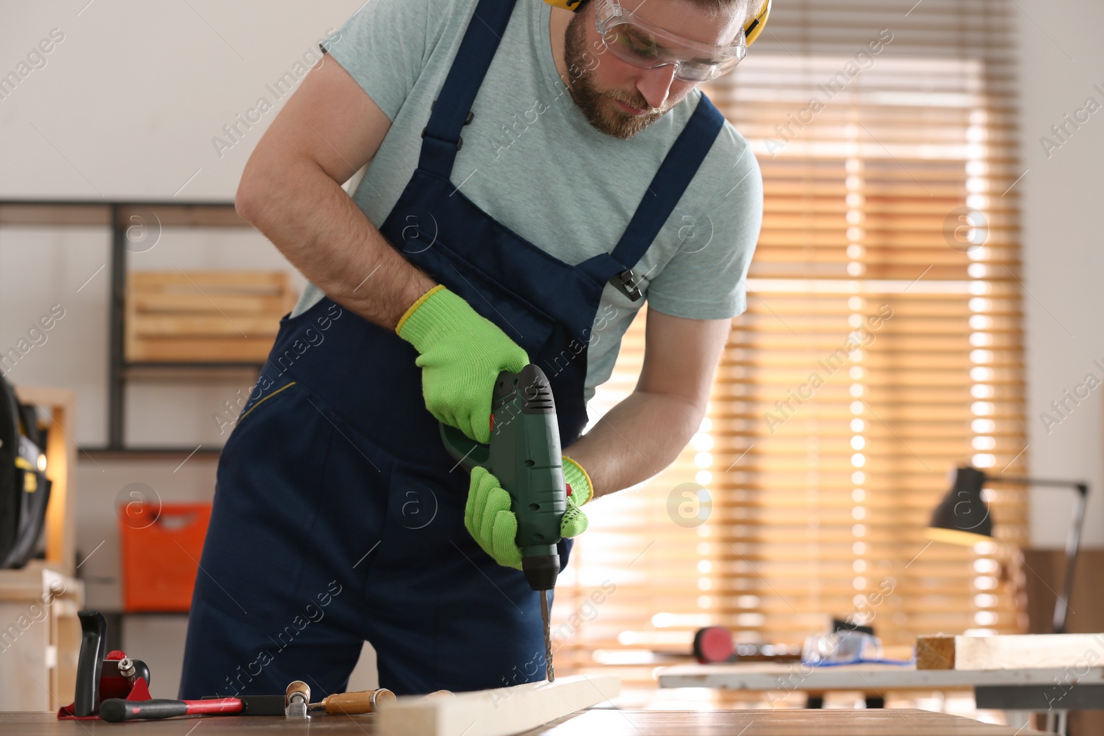 Photo of Carpenter working with electric drill at table indoors