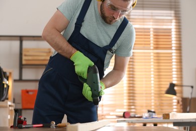Photo of Carpenter working with electric drill at table indoors