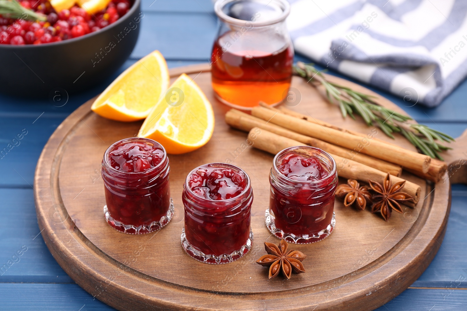 Photo of Cranberry sauce in jars and ingredients on blue wooden table, closeup