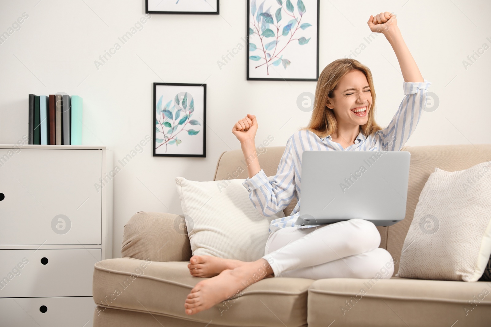 Photo of Emotional young woman with laptop sitting on sofa at home