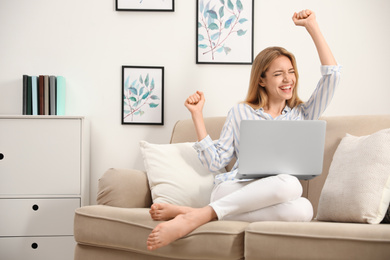 Emotional young woman with laptop sitting on sofa at home