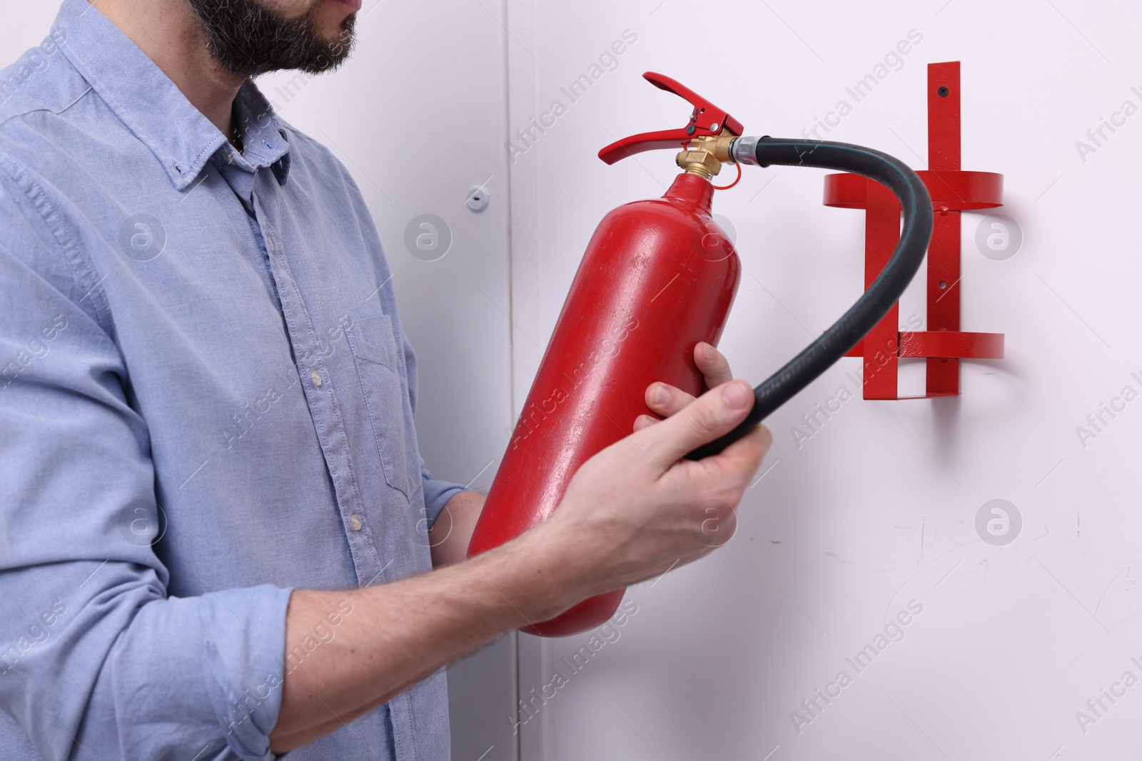 Photo of Man checking quality of fire extinguisher indoors, closeup